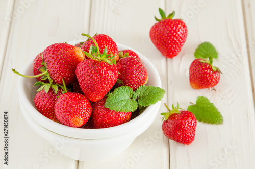 Fresh ripe strawberries in a bowl on a white wooden background.