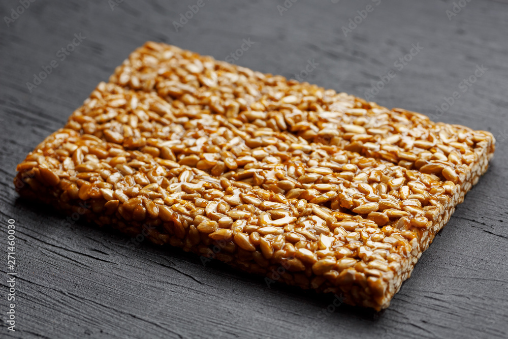 Tile kozinaki from sunflower seeds on a black textural background. Delicious oriental sweets Gozinaki from sunflower seeds, sesame seeds and peanuts, covered with honey with a shiny icing Tile kozinaki from sunflower seeds on a black textural background. Delicious oriental sweets Gozinaki from sunflower seeds, sesame seeds and peanuts, covered with honey with a shiny icing