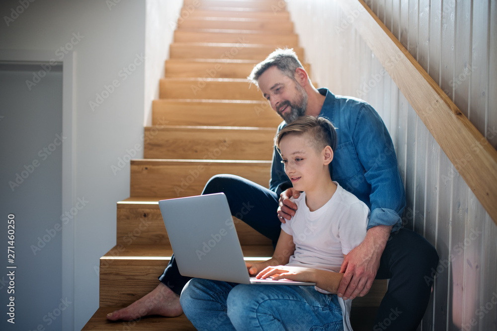Mature father with small son sitting on the stairs indoors, using laptop. Mature father with small son sitting on the stairs indoors, using laptop.