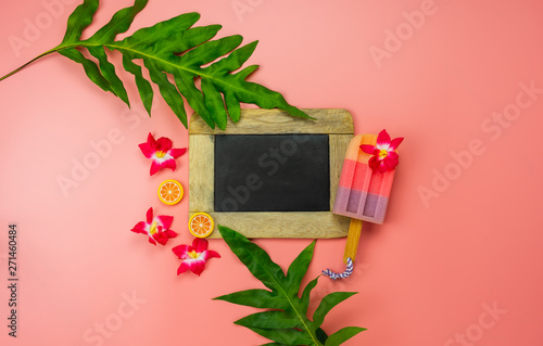 Table top view accessory plan to travel beach in summer holiday background concept.Flat lay palm leaf with many essential items ice cream & flower on modern pink paper.Blackboard for design text