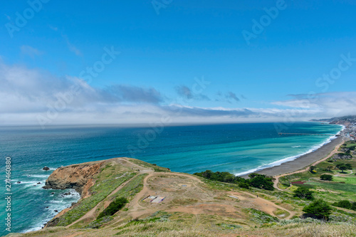 A bird's-eye view of Pacific ocean coast near Pacifica on a cloudy day with stunning view of seascape, sea cliff, sandy beach and fishing pier