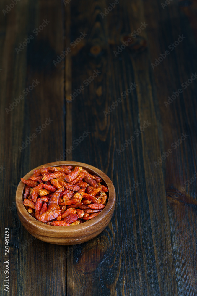 Dried bird's eye chili peppers in a wooden bowl. Dark wooden table, high resolution, negative space