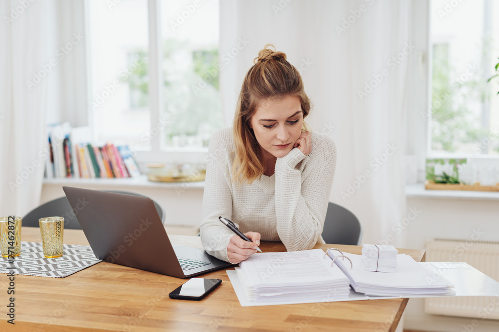 frau sitzt konzentriert am tisch und arbeitet mit laptop und unterlagen frau sitzt konzentriert am tisch und arbeitet mit laptop und unterlagen