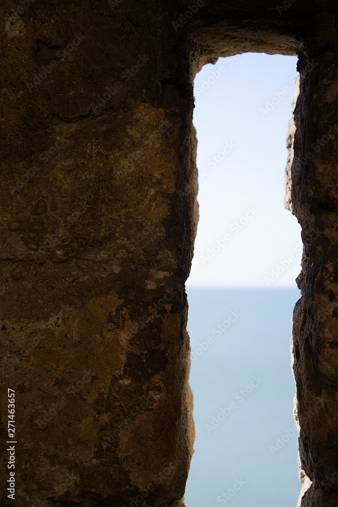 narrow long vertical security window of the fortress overlooking the sea with the horizon in the blur