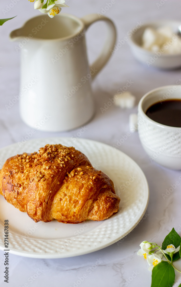 A croissant and coffee on a marble background. The flowers. Breakfast. A croissant and coffee on a marble background. The flowers. Breakfast.