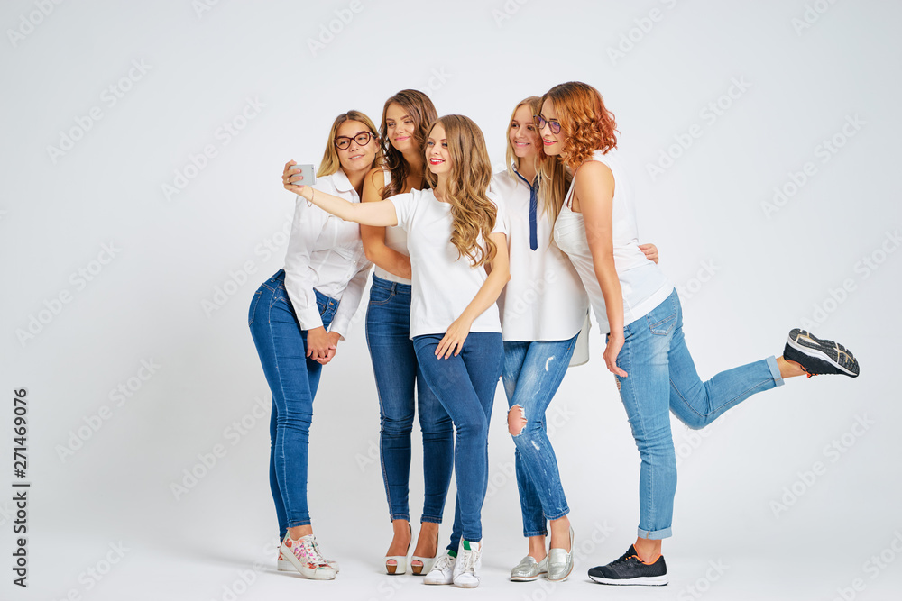 Youth and technology. Full length studio portrait of five beautiful young women laughing and taking selfie on smartphone together. Youth and technology. Full length studio portrait of five beautiful young women laughing and taking selfie on smartphone together.