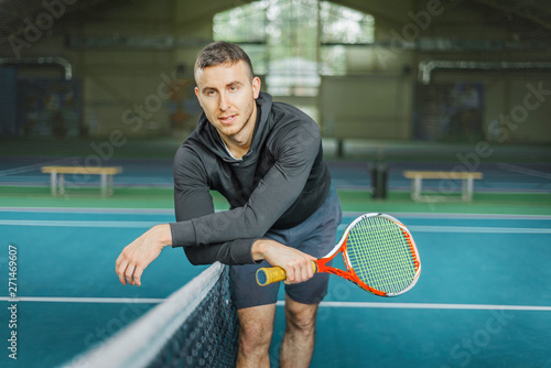 portrait of a male tennis player. young guy near the net on the court holding a racket in his hands.
