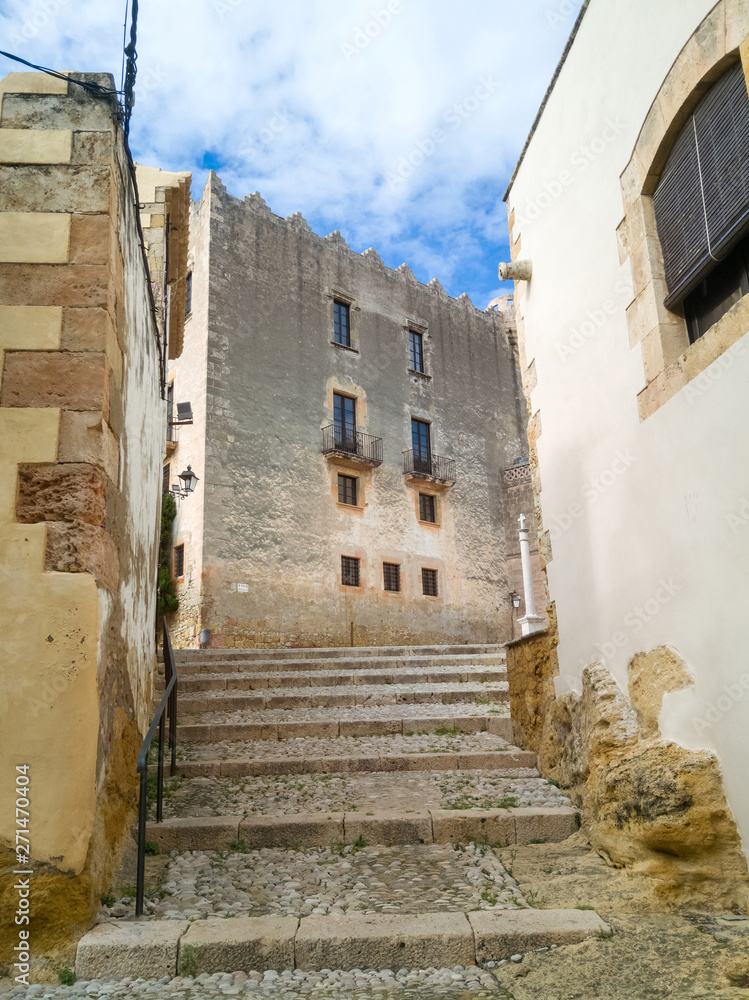 Calle en cuesta, con escaleras empedradas, de la localidad de  Altafulla con el castillo al fondo