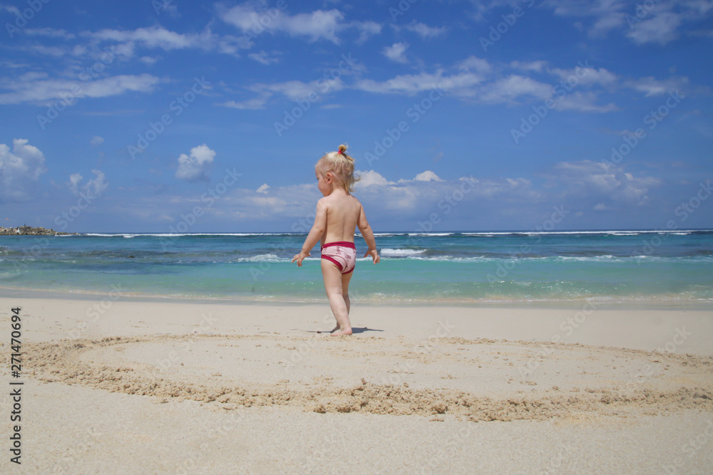 Back view of playful toddler girl on the white sandy beach looking at the horizon Back view of playful toddler girl on the white sandy beach looking at the horizon