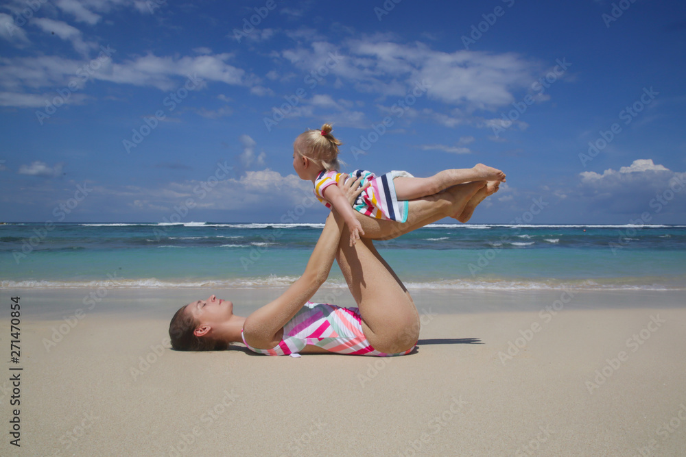 Mother doing yoga exercise together with her baby girl, outdoor family activity, family summer vacation concept Mother doing yoga exercise together with her baby girl, outdoor family activity, family summer vacation concept