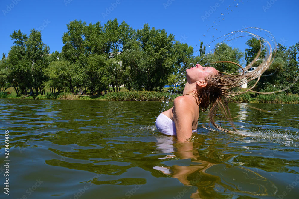Fototapeta premium Young woman raises her hair from the water on the lake