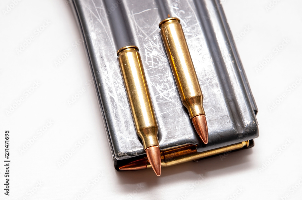 A metal 223 caliber rifle magazine loaded with 223 caliber bullets with two bullets on top of it isolated on a white background A metal 223 caliber rifle magazine loaded with 223 caliber bullets with two bullets on top of it isolated on a white background