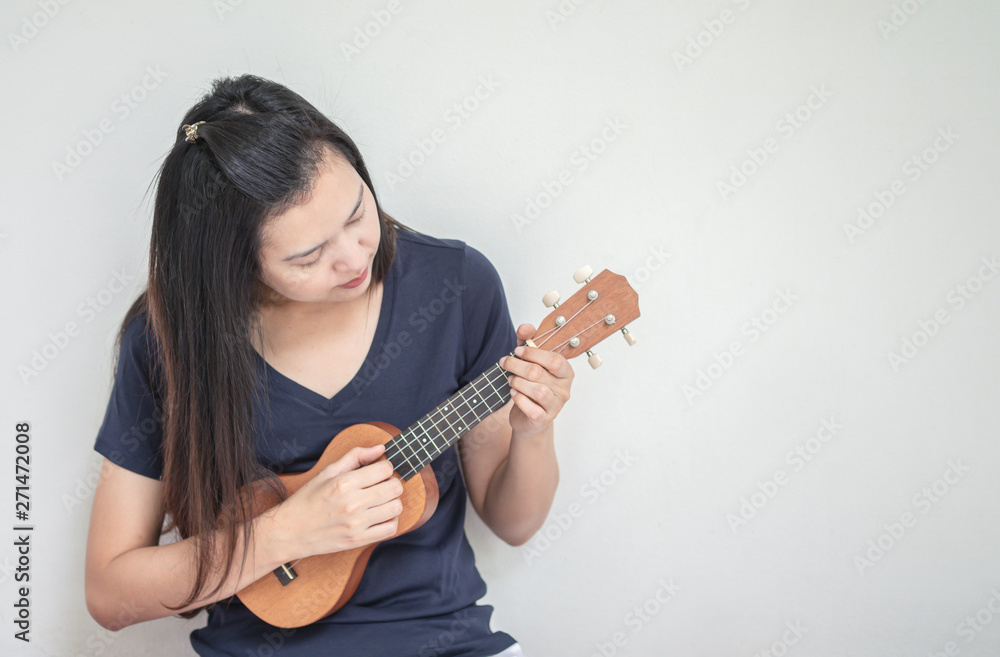 Closeup asian woman playing ukulele on white cement wall texture background with copy space Closeup asian woman playing ukulele on white cement wall texture background with copy space
