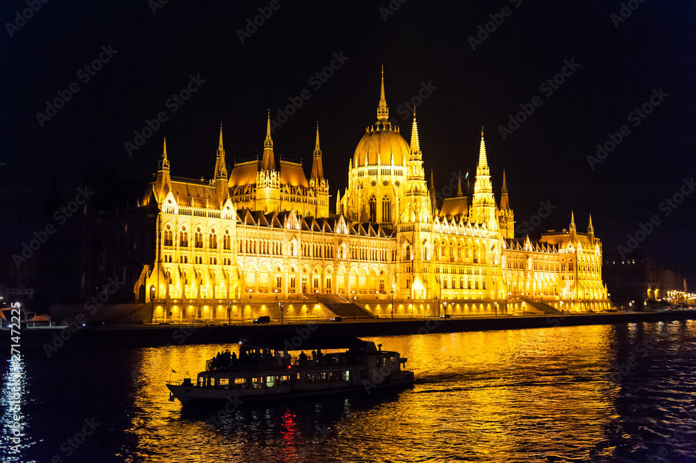 Budapest's famous parliament buildings at night, with a silhoutte of a riverboat in front of it.