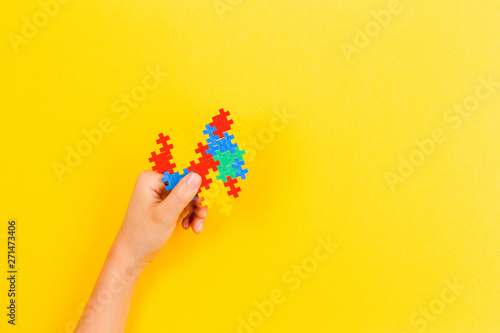 Child hand holding colorful heart on yellow background. World autism awareness day concept