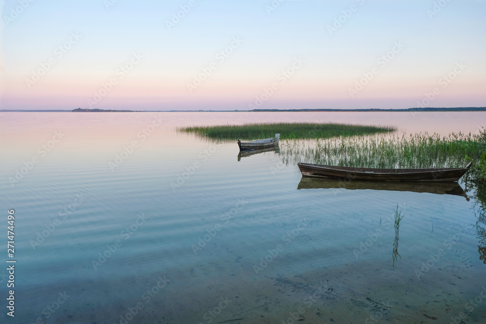Wooden boats in a reed on the dawn background. Still on the lake Svityaz. Ukrainian nature.