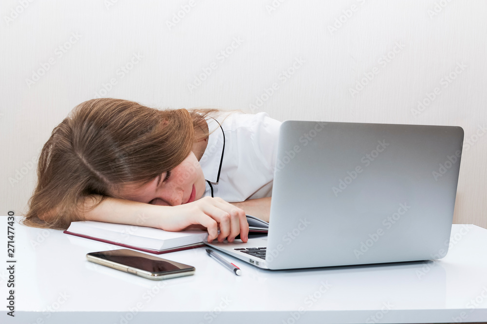 Young girl with blond hair in a white blouse put her head on the table in front of a laptop Young girl with blond hair in a white blouse put her head on the table in front of a laptop