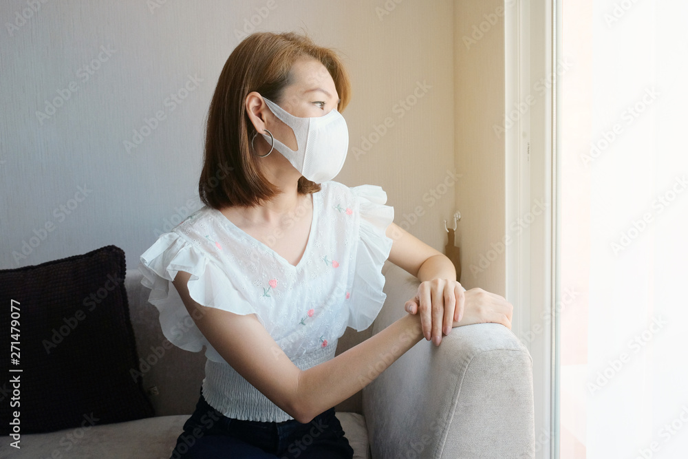 Portrait of young Asian woman wearing face mask sitting near window Portrait of young Asian woman wearing face mask sitting near window