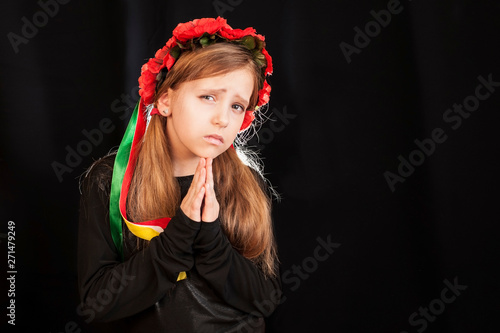 A sad girl prays on a dark background. The girl prays for no war on the whole earth