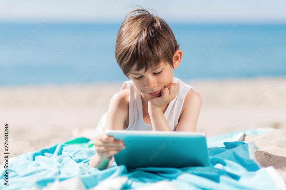 Boy with tablet lying on the beach a sunny day