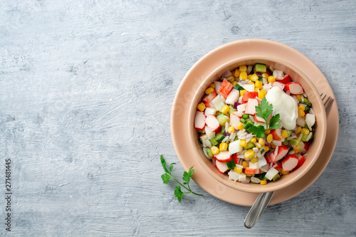 Salad with crab sticks, sweet corn, cucumbers, boiled eggs, onion and rice in bowl on concrete background. Russian cuisine. Top view. Copy space.