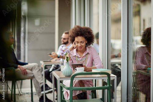 Smiling grogeous mixed race woman in pink striped dress sitting in cafe and using tablet. On table are cup of coffee, book and lemonade. photo