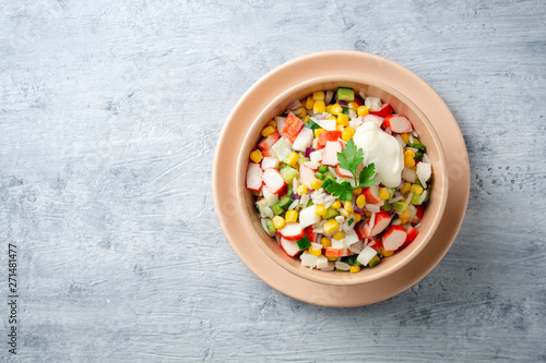 Salad with crab sticks, sweet corn, cucumbers, boiled eggs, onion and rice in bowl on concrete background. Russian cuisine. Top view. Copy space.
