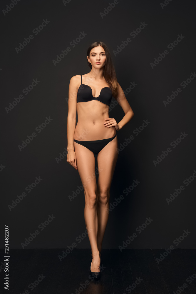 Beautiful slim model with healthy tan skin in black swimsuit on dark background.
