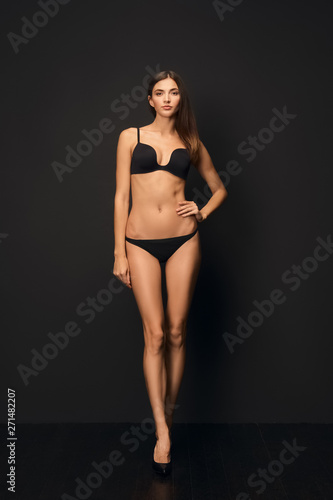 Beautiful slim model with healthy tan skin in black swimsuit on dark background. © boomeart