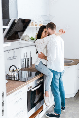 happy woman sitting on table at kitchen and embracing man