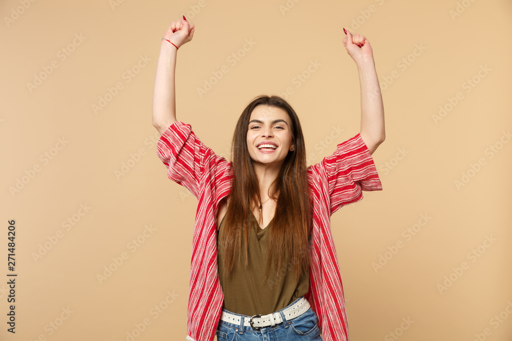 Portrait of smiling young woman in casual clothes rising hands, clenching fists like winner isolated on pastel beige wall background. People sincere emotions, lifestyle concept. Mock up copy space. Portrait of smiling young woman in casual clothes rising hands, clenching fists like winner isolated on pastel beige wall background. People sincere emotions, lifestyle concept. Mock up copy space.