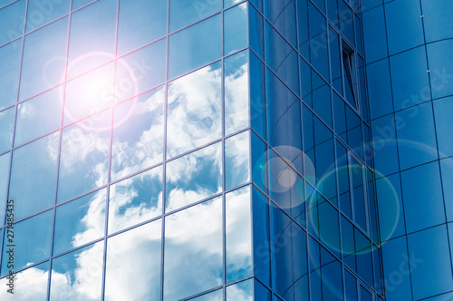 Glass windows of modern building with reflecting blue sky and clouds.