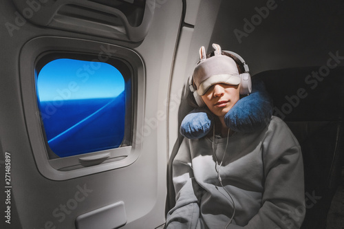 Asian girl sleeping in her seat on the plane near the window in a mask and with a pillow to sleep. The concept of travel with comfort and jetlag photo