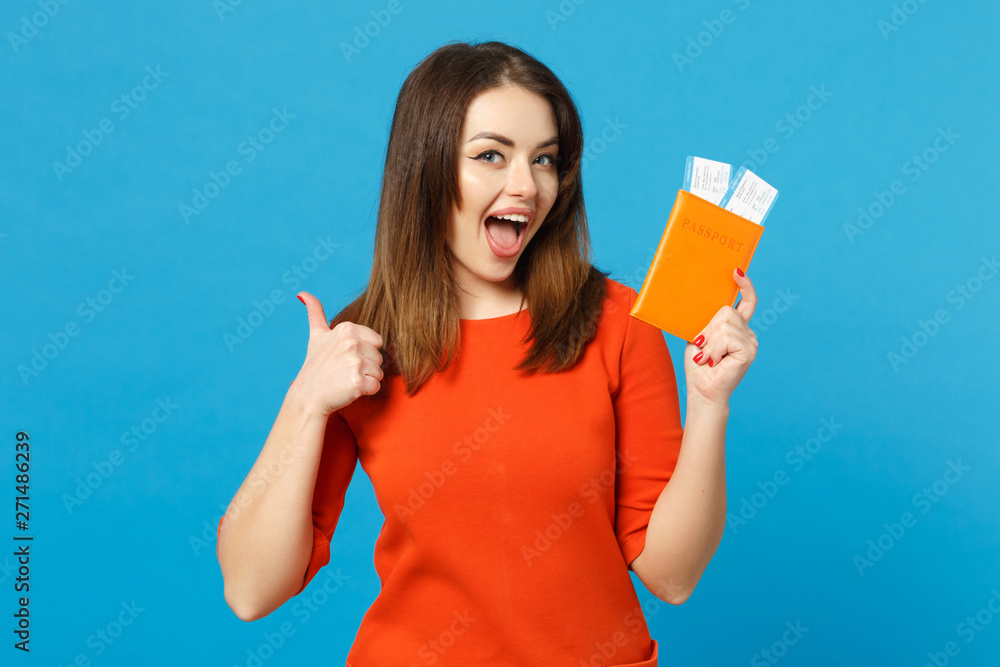Beautiful brunette young woman wearing red orange dress hol in hand passport tickets isolated over trendy blue wall background, studio portrait. People lifestyle fashion concept. Mock up copy space. Beautiful brunette young woman wearing red orange dress hol in hand passport tickets isolated over trendy blue wall background, studio portrait. People lifestyle fashion concept. Mock up copy space.