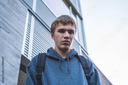 Sad teenager standing next to a school on an overcast day.