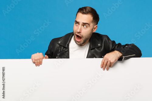 Handsome young bearded man hold big white empty blank billboard for promotional content isolated on blue wall background studio portrait. People sincere emotions lifestyle concept. Mock up copy space.