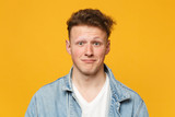 Portrait of funny perplexed young man wearing denim casual clothes looking camera isolated on yellow orange wall background in studio. People sincere emotions, lifestyle concept. Mock up copy space.