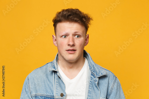 Portrait of shocked scared young man wearing denim casual clothes looking aside isolated on yellow orange wall background in studio. People sincere emotions, lifestyle concept. Mock up copy space.