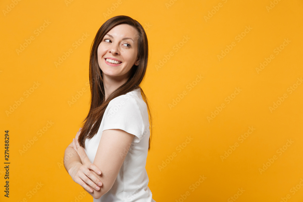 Obraz premium Side view of smiling young woman in white casual clothes holding hands crossed, looking aside isolated on bright yellow orange wall background in studio. People lifestyle concept. Mock up copy space.