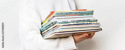 Girl in a white woolen sweater holding a stack of children's books on white background with copy space. Long wide banner
