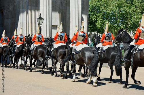 Royal guards on horseback dressed in ceremonial red coats pass in a parade - uk