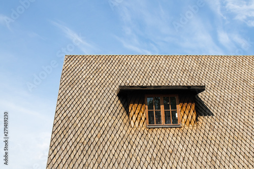 Steep old shingle roof with a window against blue sky