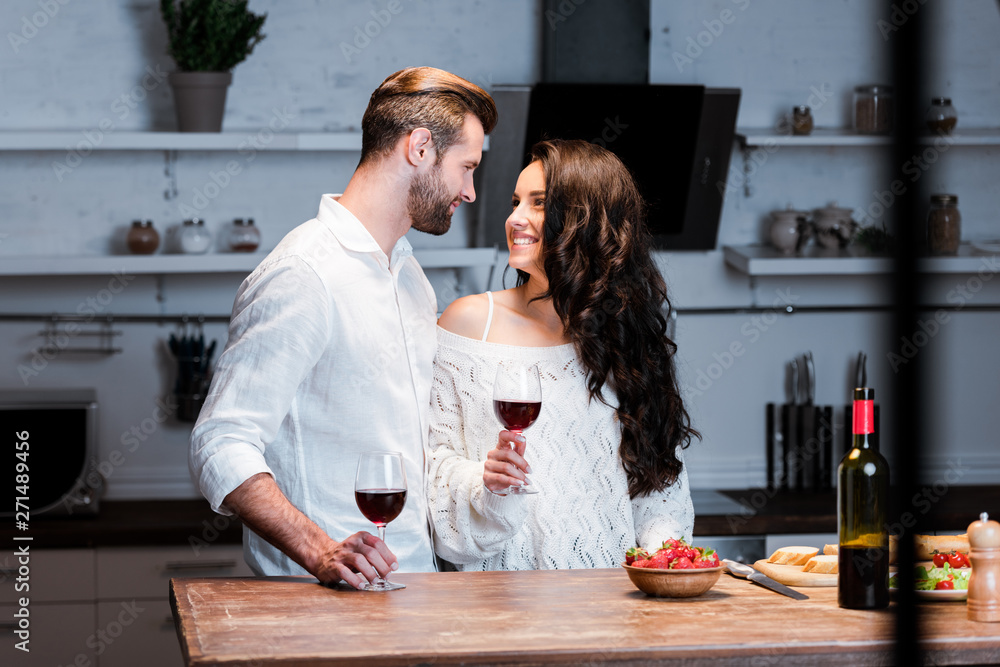 happy couple holding glasses with red wine and looking at each other happy couple holding glasses with red wine and looking at each other