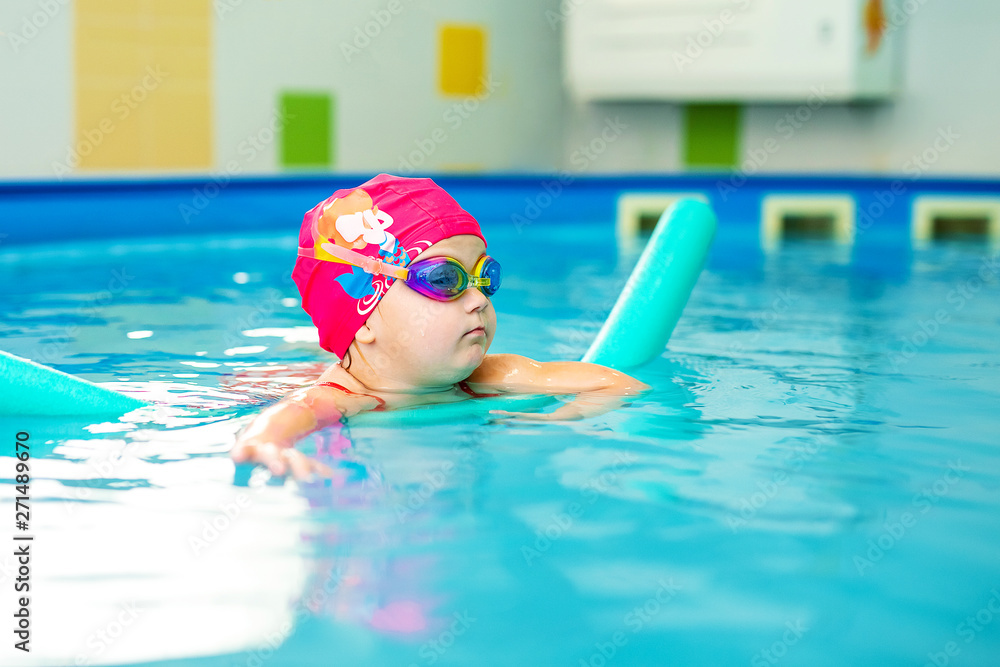 Cute baby girl in red swimsuit and special glasses playing in the pool