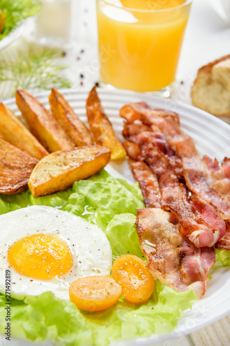 Fried bacon with French fries and tender egg, and a glass of fresh juice.