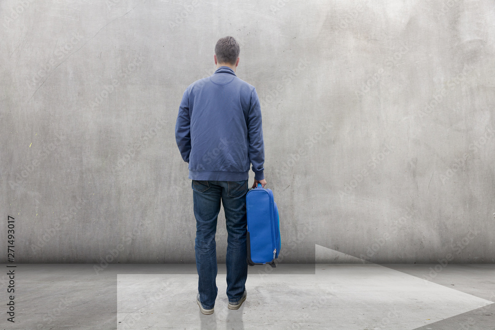 Mann mit Reisekoffer steht vor einer Wand Mann mit Reisekoffer steht vor einer Wand