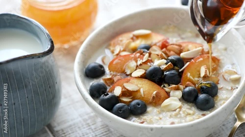 Pouring maple syrup on breakfast porridge with fruits and nuts. Concept of healthy eating, dieting, healthy lifestyle