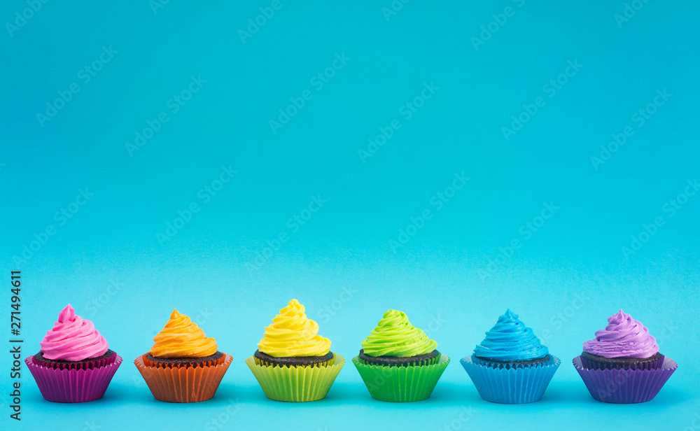 Rainbow Colored Frosted Chocolate Cupcakes on Teal Background Rainbow Colored Frosted Chocolate Cupcakes on Teal Background