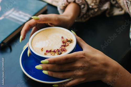 Coffee cup with latte art on wooden background in female hands. Beautiful foam, brown ceramic cup, space for text and design.