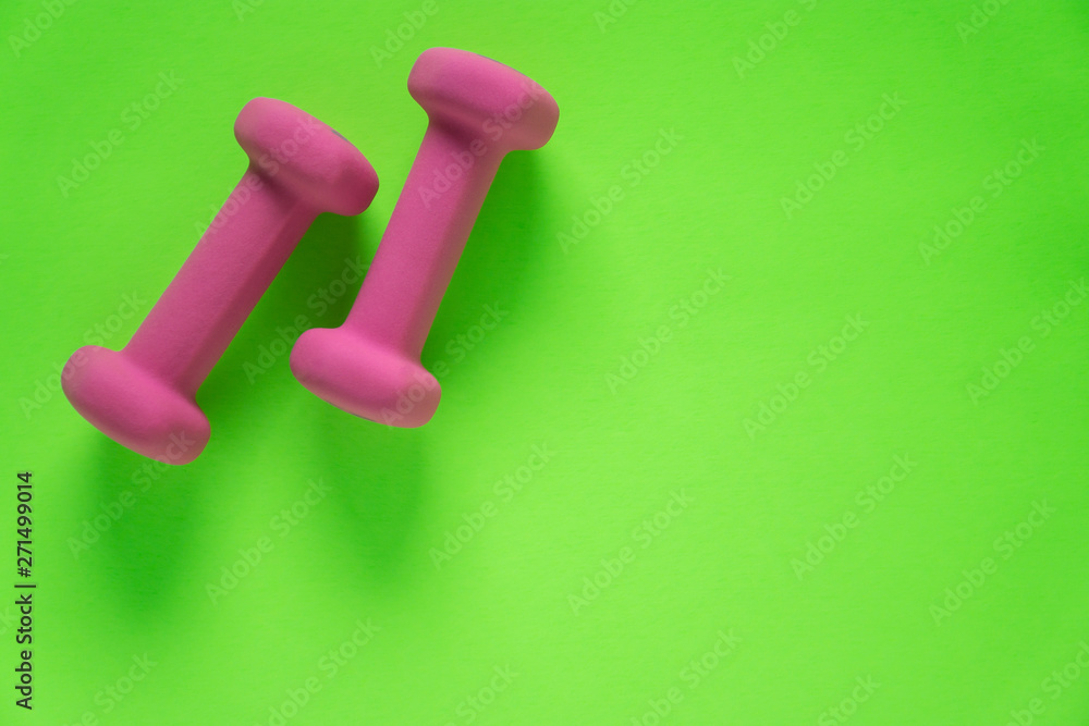Fitness equipment with womens pink weights/ dumbbells isolated on a lime green background with copyspace Fitness equipment with womens pink weights/ dumbbells isolated on a lime green background with copyspace